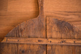 Vintage wooden pizza board showing rustic patina, central split, and hand-hewn nails.