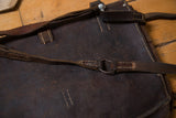 Detail of dark brown vintage leather messenger bag, showing aged texture, stitching, and metal ring.