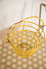 Small vintage yellow egg basket, showcasing its chipped mustard paint and rust patina.
