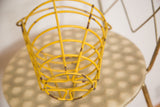 Vintage yellow egg basket, close-up showing worn mustard paint and aged rust on metal wires.