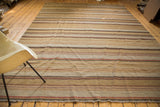 Hand woven kilim rug end with muted stripes, coarse texture, and decorative fringe.