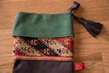 Green suede cuff, antique rug fragment, and black leather tassel on a charcoal stocking.