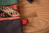 Embossed red leather brand tag on the charcoal linen body of a rug fragment stocking.