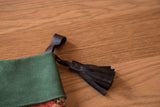 Handmade black leather tassel attached to the green suede cuff of a luxe stocking.