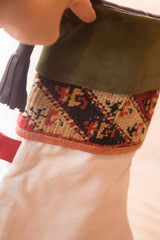 Olive green suede cuff, black leather tassel, geometric black and rust rug fragment.