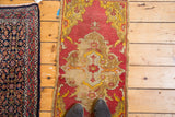 Distressed Turkish Yastik rug with worn saffron yellow and brick red medallion, shoes visible.