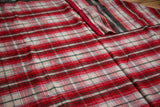 Folded vintage wool blanket with classic red, green, blue plaid pattern and red satin edge.