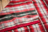 Vintage wool blanket detail showing plaid pattern in red, green, blue with red satin edging.