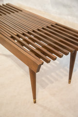 Mid-century modern expandable wood slat bench with tapered leg and brass cap.