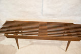 Angled view of the vintage MCM expandable slat bench, showing overlapping brown wooden slats.