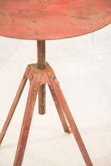 Patinaed reddish-brown metal tripod base with visible rivets on the vintage industrial table.