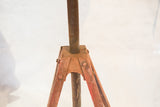 Close-up of the table's industrial rusted metal tripod base with faded orange paint.