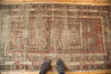 Distressed geometric motifs and serpent border of this Antique Caucasian rug in muted red and ivory, with feet.