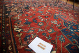 Close-up of distressed vintage Bakhtiari carpet, featuring rectilinear patterns in brick red and indigo blue.