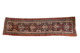 Uneven Vintage Caucasian runner rug, repeating tribal medallions in madder red, teal, and bronze.