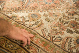 Hand on distressed antique Mahal carpet, highlighting faded peach and ivory patina.