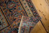Folded edge of an antique distressed Doroksh rug revealing its intricate rust and navy border.