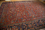 Distressed vintage Heriz rug with brick red field and colorful sickle-shaped serrated leaves.