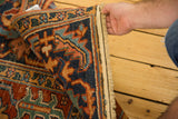 Secured edge and fringe of a distressed Heriz rug, with navy and red tones.