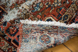 View of the tightly woven back, white fringe, and distressed red and blue pile of a Heriz rug.