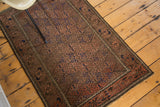 Distressed Belouch rug showing detailed geometric diamond gul patterns in muted madder red, navy, and brown.