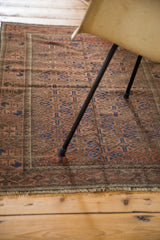 Distressed Belouch rug, geometric diamond gul pattern in faded madder, copper, navy, and fringe.