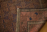 Vintage distressed Belouch rug corner, revealing hand-knotted texture, fringe, and red-brown-blue gul design.