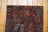 Feet on vintage Sarouk rug, highlighting cherry red field with intricate floral design.