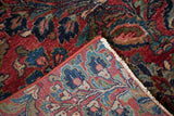 Folded vintage Sarouk rug shows cherry red floral pile and hand-knotted back weave.