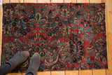 Vintage Sarouk fragment rug with cherry red field, intricate floral patterns, feet for scale.