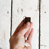 Small, dark brown reclaimed leather miniature book necklace held in hand, showing fine texture.