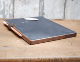 Dark reclaimed wood edge of chalkboard pad with leather strap holding two chalk pencils.