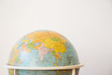 Vintage 1970s tin globe, detailed view of Asian continent, muted yellow and blue.