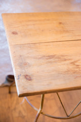 Reclaimed wood tabletop corner showing light grain, natural knots, and part of the yellow metal base.