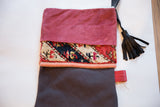 Close-up of a fuchsia suede cuff, antique rug fragment, and black leather tassel.
