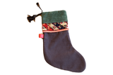 Black linen holiday stocking with a green suede cuff, a colorful antique rug fragment, and a leather tassel.