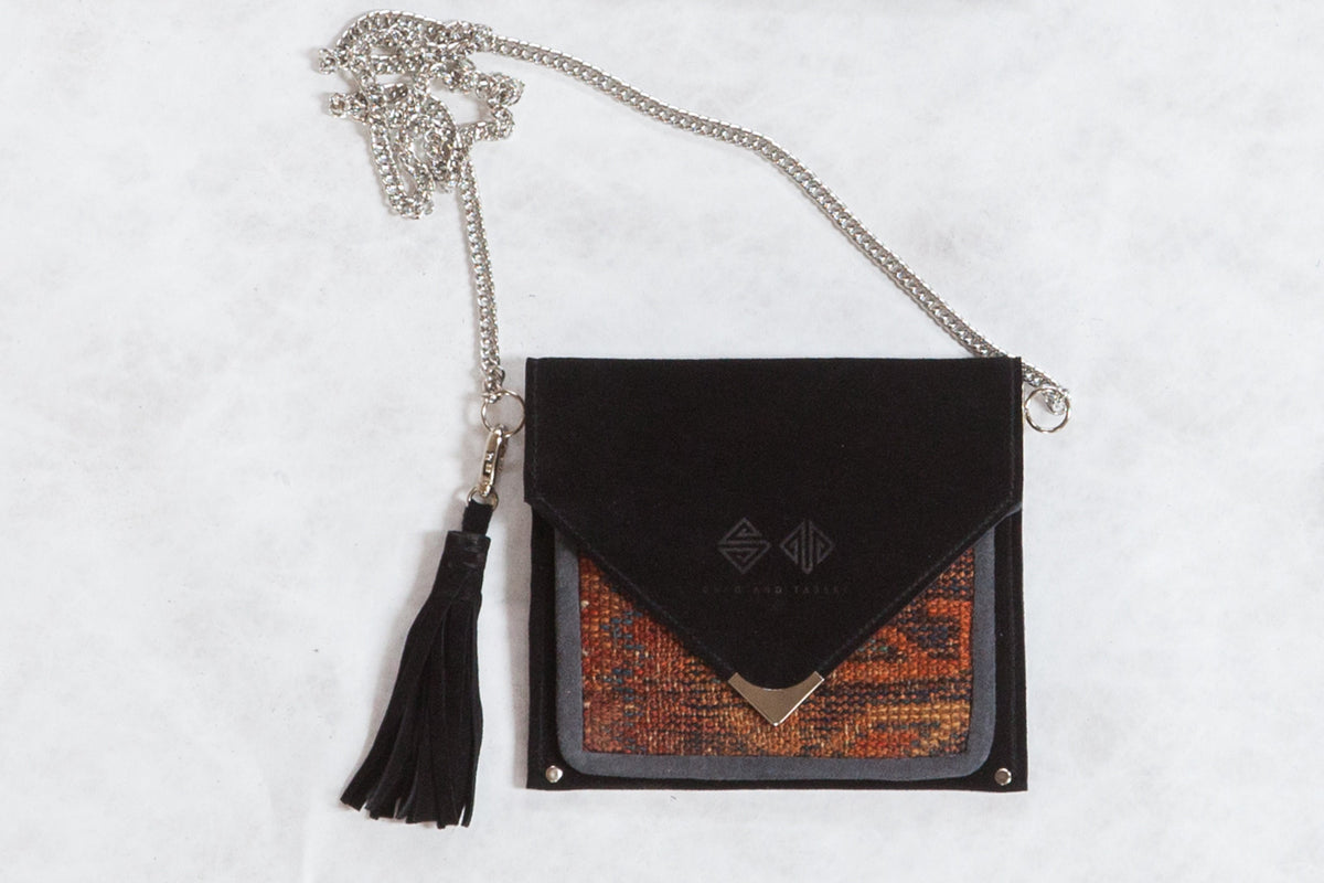 Antique Kurdish rug fragment purse with a black suede flap, tassel, and silver chain.