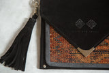 Embossed brand logo on the black suede flap and matching tassel of the rug handbag.