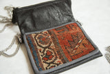 Hand-knotted antique Kurdish rug fragment on purse, featuring geometric patterns in rust, blue, and cream.