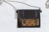 Antique Caucasian rug fragment bag with black leather flap, geometric design, and silver chain strap.