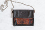 Antique Kurdish rug fragment bag with dark leather, silver chain, and geometric rust and blue pattern.
