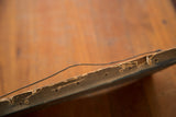 Worn back edge of the vintage sea painting's frame with hanging wire.