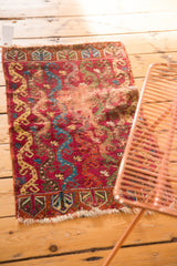 Antique Yastic rug corner shows germinating plant border, tattered fringe, and worn raspberry red field.