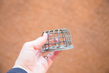 A hand holding a small vintage flower frog with an industrial green metal cage design.