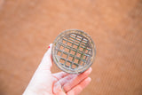 The gridded top of a vintage flower frog with aged metal patina and embossed lettering.