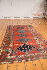 Antique Persian Bijar runner with geometric diamond medallions on cherry red, showing tattered edges.
