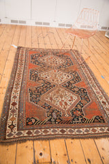 Antique Qashqai rug corner: tribal motifs, madder red, deep navy, ivory, visible wear, and fringe.
