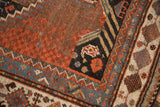 Antique Qashqai rug close-up: madder red field, navy corner with stylized bird, complex tribal borders.