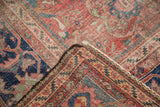 Folded corner of vintage Mahal carpet showing intricate red, blue, and faded neutral floral patterns.