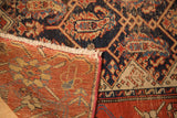 Antique Hamadan rug construction detail: dark blue geometric pile, worn fringe, and red woven foundation.
